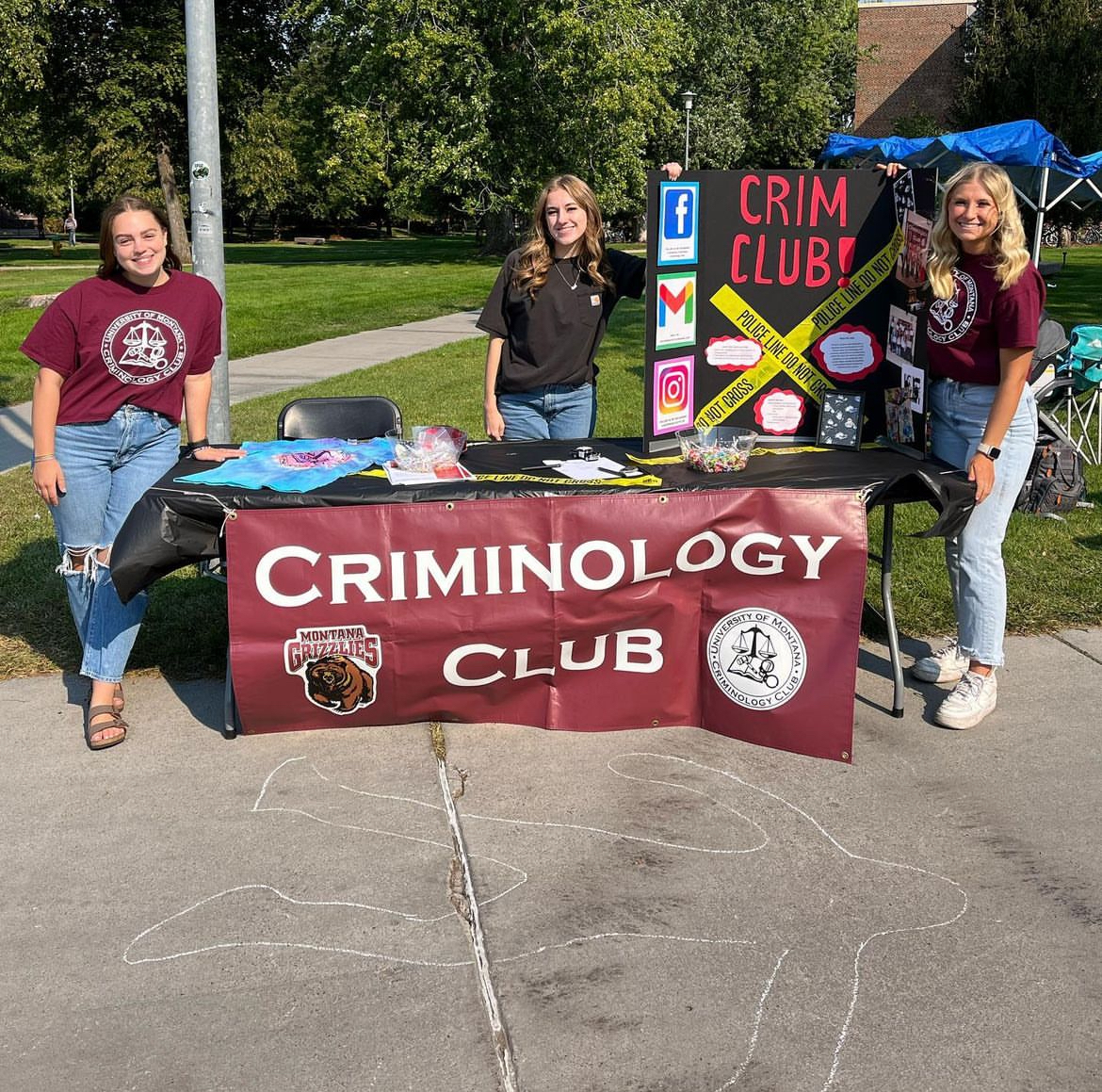 Crim Club students at an informational booth with a chalk outline drawn on the ground at a student welcome event.