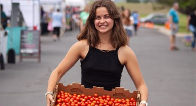 UM sociology major Keeza Leavens holds a box of tomatoes at the farmers' market for her internship focusing on food insecurity in Montana.