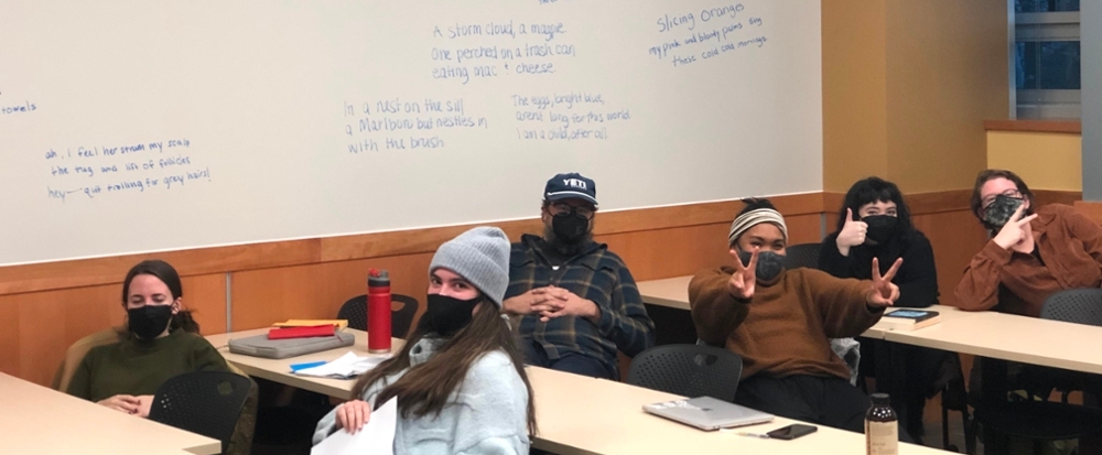 University of Montana MFA students smile in the classroom in front of a board with poetry snippets.