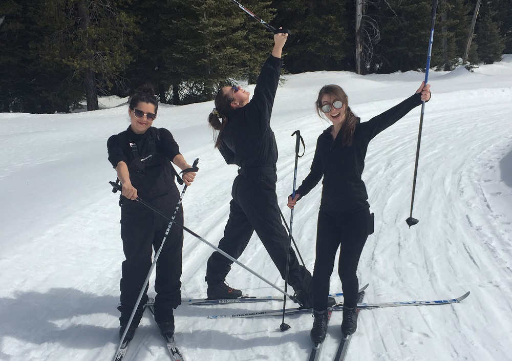 MFA alumni Nicole Gomez, Danielle Cooney, and Beatrice Garrard posing in skis on a snowy path.