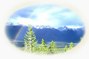 large valley with pine trees, a rainbow, and mountains in the distance