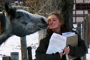 woman with clipboard getting nuzzled by horse