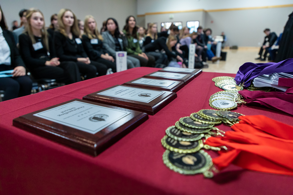 awards and picture sit on a table in front of a group of sitting students.