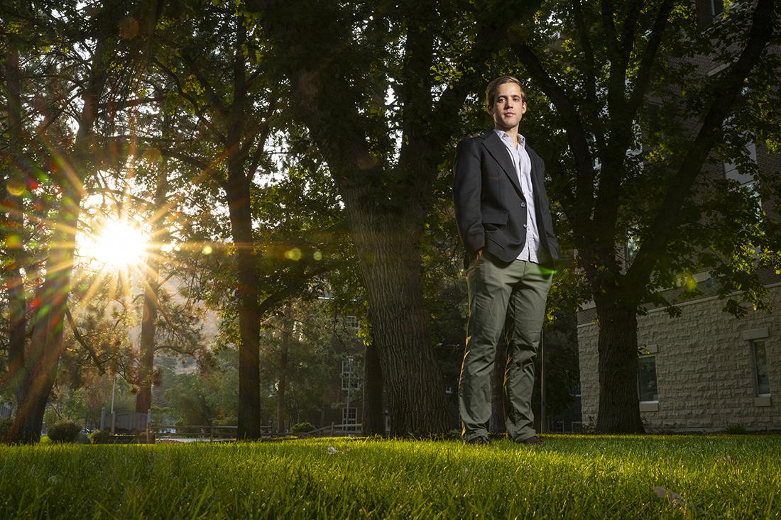 Student, Luke Santore, standing under trees with sun shining through the leaves.